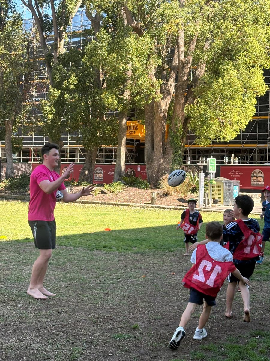Coach Jo passing a rugby ball to kids in red bibs